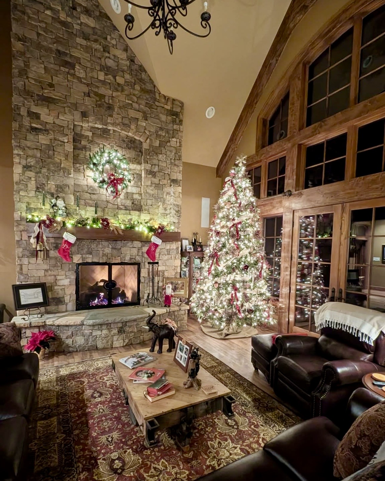 A great room glowing for Christmas with a lit tree, fireside stockings, wreath, and garland