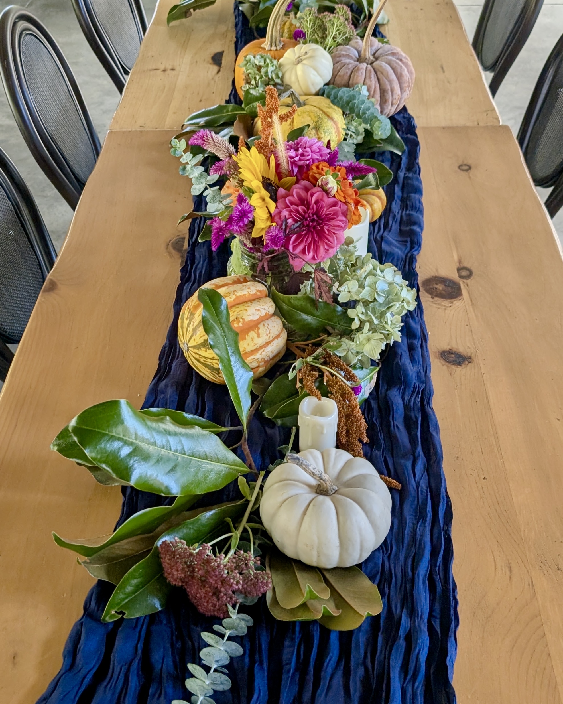 A harvest table runner of magnolia, hydrangea, dahlias, and heirloom pumpkins on navy linen